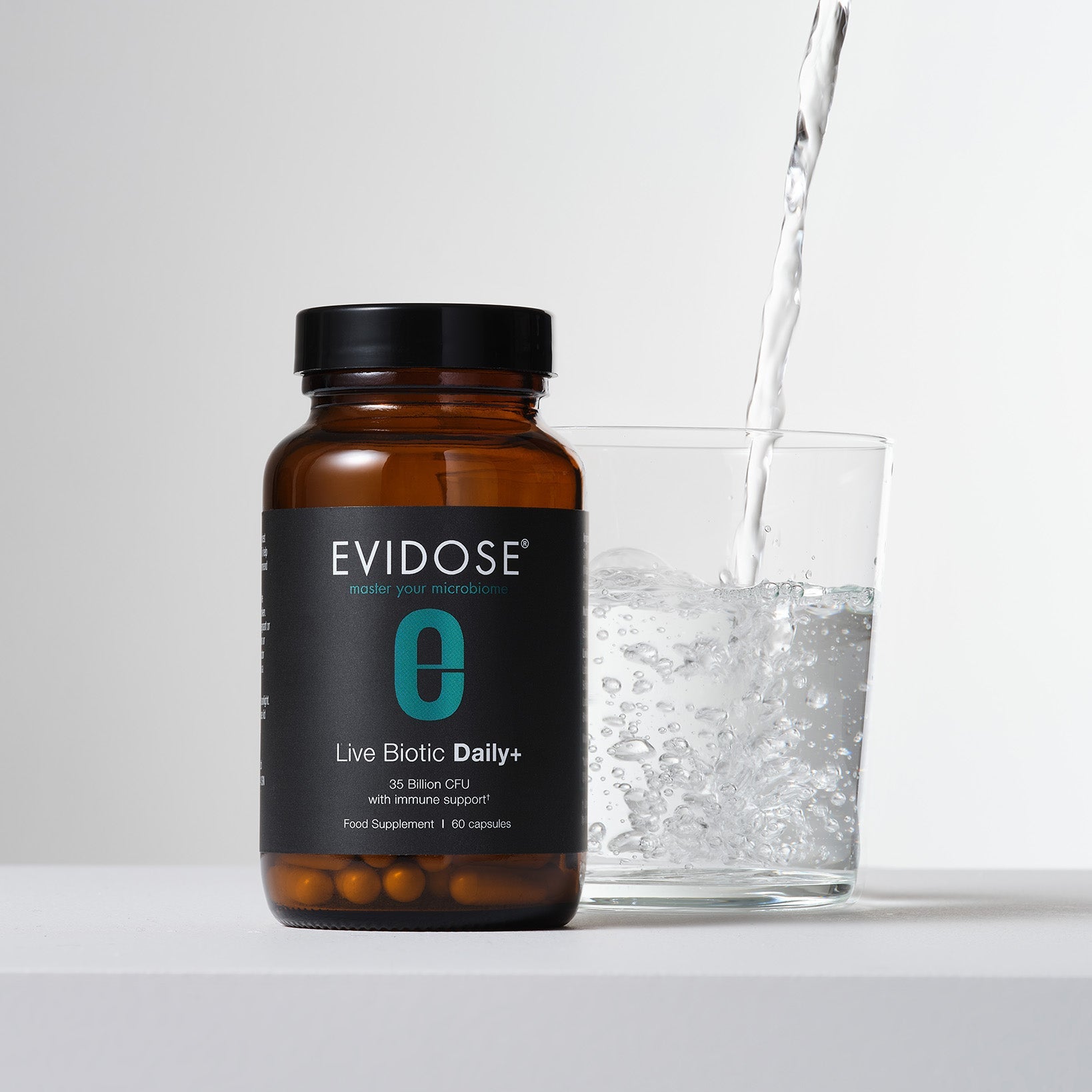 Evidose supplement bottle with a glass of water being poured into it on a light background